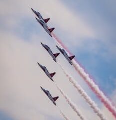 Five jets performing synchronized aerobatic maneuvers against a blue sky.